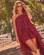 Woman in burgundy tiered ruffle maxi dress with cowboy boots and aviator sunglasses at sunny ranch setting