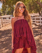 Woman in burgundy boho strapless ruffle mini dress with aviator sunglasses, smiling outdoors near white fence