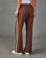 Brown wide-leg track pants with cream side stripes, elastic waistband, worn with white sneakers, back view