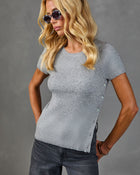 Woman wearing gray ribbed knit short-sleeve top with side buttons, paired with dark jeans and round tortoise sunglasses