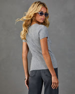 Woman wearing fitted gray ribbed short-sleeve knit top with gold buttons, dark wide-leg jeans, tortoise sunglasses, gold hoop earrings