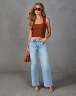 Woman wearing brown ribbed crop tank top, light wash wide-leg jeans, nude strappy heels, and tortoise sunglasses holding brown mini bag