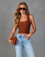Woman wearing brown ribbed knit crop tank top with square neckline, light wash jeans, cognac handbag, and tortoise sunglasses