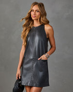 A woman modeling a sleeveless dark gray faux-leather dress with decorative stitching and side pockets, posed against a textured gray studio background.