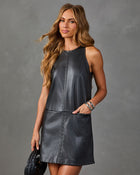 A woman modeling a sleeveless dark gray faux-leather dress with decorative stitching and side pockets, posed against a textured gray studio background.