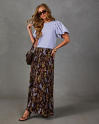 Woman in lavender puff-sleeve knit top and brown floral pleated maxi skirt with quilted crossbody bag and strappy sandals