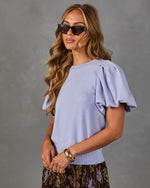 Woman wearing a lavender knit top with puff sleeves, cat-eye sunglasses, gold cuff bracelet and pleated floral midi skirt