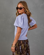 Woman in lavender puff-sleeve knit top and pleated brown floral midi skirt with cat-eye sunglasses and gold cuff bracelet