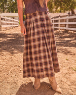 Women's plaid midi skirt in brown tartan with pleated waist, paired with tan cowboy boots at a ranch