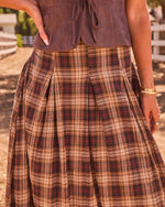 Brown plaid pleated midi skirt with red accents paired with mauve suede corset top, styled for western fall fashion