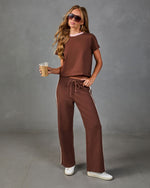 Woman wearing brown crop tee and wide-leg track pants with side stripes, holding iced coffee, white sneakers, aviator sunglasses