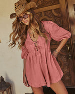 Woman wearing dusty rose lace-up babydoll mini dress with puff sleeves, woven cowboy hat, and tinted sunglasses