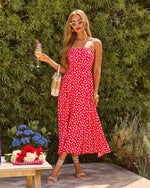 Woman in red floral midi dress, white strappy heels, cat-eye sunglasses, holding champagne at outdoor summer party