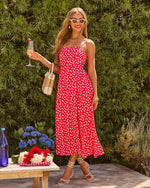 Woman in red floral midi dress with spaghetti straps holding champagne at summer garden party, white heels and sunglasses