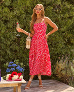 Woman in red floral midi dress, white cat-eye sunglasses, strappy heels, holding champagne at summer garden party