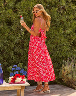 Woman in red floral midi dress with open back, holding champagne at outdoor summer party with garden backdrop
