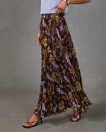 Brown pleated maxi skirt with blue and gold floral print, styled with a lavender knit top and strappy heeled sandals