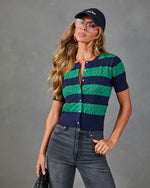 Woman wearing navy and green striped cable-knit cardigan, gray jeans, New York baseball cap, and aviator glasses