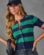 Navy and green striped cable-knit short-sleeve cardigan with pearl buttons, styled with dark jeans, baseball cap, and woven bag