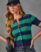 Navy and green striped cable-knit short-sleeve cardigan with pearl buttons, styled with dark jeans, baseball cap, and woven bag
