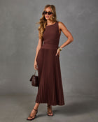Woman in a brown sleeveless pleated midi dress with sunglasses, quilted brown handbag, gold cuff and strappy black heels