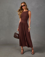 Woman in a brown sleeveless pleated midi dress with ruched waist, black cat-eye sunglasses, strappy heels and quilted bag