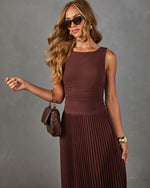 Woman in brown sleeveless pleated midi dress with ruched waist, cat-eye sunglasses, gold cuff and quilted brown chain bag