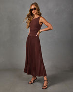 Woman in a brown sleeveless pleated midi dress with ruched waist, black cat-eye sunglasses, gold cuff and strappy heeled sandals