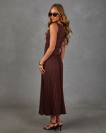 Woman in a brown sleeveless pleated midi dress with ruched waist, gold cuff bracelet, sunglasses and strappy black heeled sandals