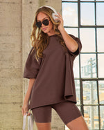 Woman wearing chocolate brown oversized t-shirt and matching bike shorts set with white headphones and sunglasses