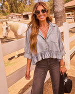 Smiling woman in chambray ruffle crop top, dark jeans, and sunglasses leaning on white fence at sunny ranch with white horse