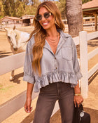 Woman in cropped chambray ruffle top and dark jeans smiling at ranch with white horse and white fence