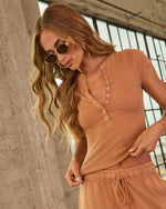 Woman wearing terracotta ribbed henley crop top with snap buttons and matching drawstring shorts, gold sunglasses