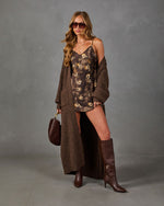 Woman in brown floral satin slip dress, long chunky knit cardigan, knee-high leather boots and sunglasses holding a maroon bag
