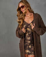 Woman wearing a brown knit longline cardigan over a floral satin slip dress with aviator sunglasses and layered necklaces