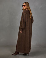 Woman in a long brown ribbed knit maxi cardigan with balloon sleeves, aviator sunglasses and brown heeled knee-high boots