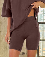 Woman wearing matching dark brown biker shorts and oversized t-shirt set, high waist elastic waistband, fitted athleisure style