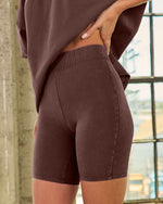 Women's dark brown acid-wash biker shorts with wide ribbed waistband, shown from behind with matching oversized tee