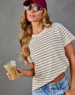 Woman in cream striped crop tee, burgundy baseball cap, sunglasses, holding iced coffee, paired with light wash jeans