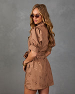 A woman modeling a brown mini dress with a subtle leopard print pattern, puff sleeves, and a tie waist, posed against a textured gray studio background.