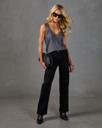 Woman wearing gray lace cami top, black wide-leg jeans, ankle boots, holding woven clutch, gold jewelry, oversized sunglasses
