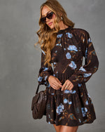 Woman in a brown floral mini dress with blue roses, long puff sleeves, tiered skirt, sunglasses and a woven brown shoulder bag