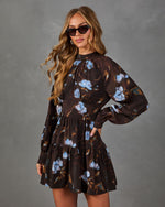 Woman in a brown long-sleeve tiered mini dress with blue floral print, high neckline, and cat-eye sunglasses