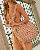 Woman wearing tan ribbed henley bodysuit and drawstring joggers carrying a quilted puffer crossbody tote bag in blush beige