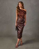 Woman in a brown satin asymmetrical off-shoulder top and chocolate faux leather midi skirt with strappy heels and clutch