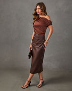 Woman in a brown satin off-shoulder top and chocolate faux leather midi skirt with strappy heeled sandals and gold cuff bracelet