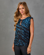 Woman wearing teal black abstract print sleeveless blouse with tie neckline, paired with black pants