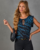 Woman wearing blue black abstract print tie-neck blouse, black skinny jeans, gold belt, holding woven leather bag