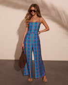 Woman wearing blue floral stripe wide-leg jumpsuit with spaghetti straps, paired with sandals and woven bag