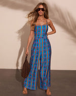 Blue floral stripe wide-leg jumpsuit with spaghetti straps, styled with gold hoops, layered necklaces, and woven bag